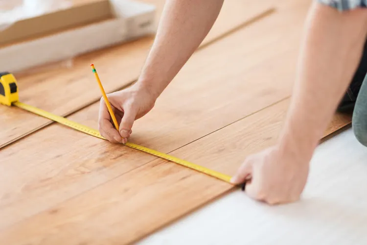 A builder measuring a floor with a tape measure and pencil