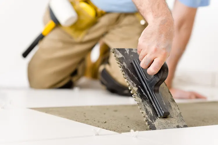 A worker spreading tile adhesive with a notched trowel